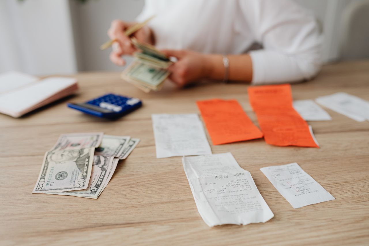 A person using a calculator and cash to plan a household budget.