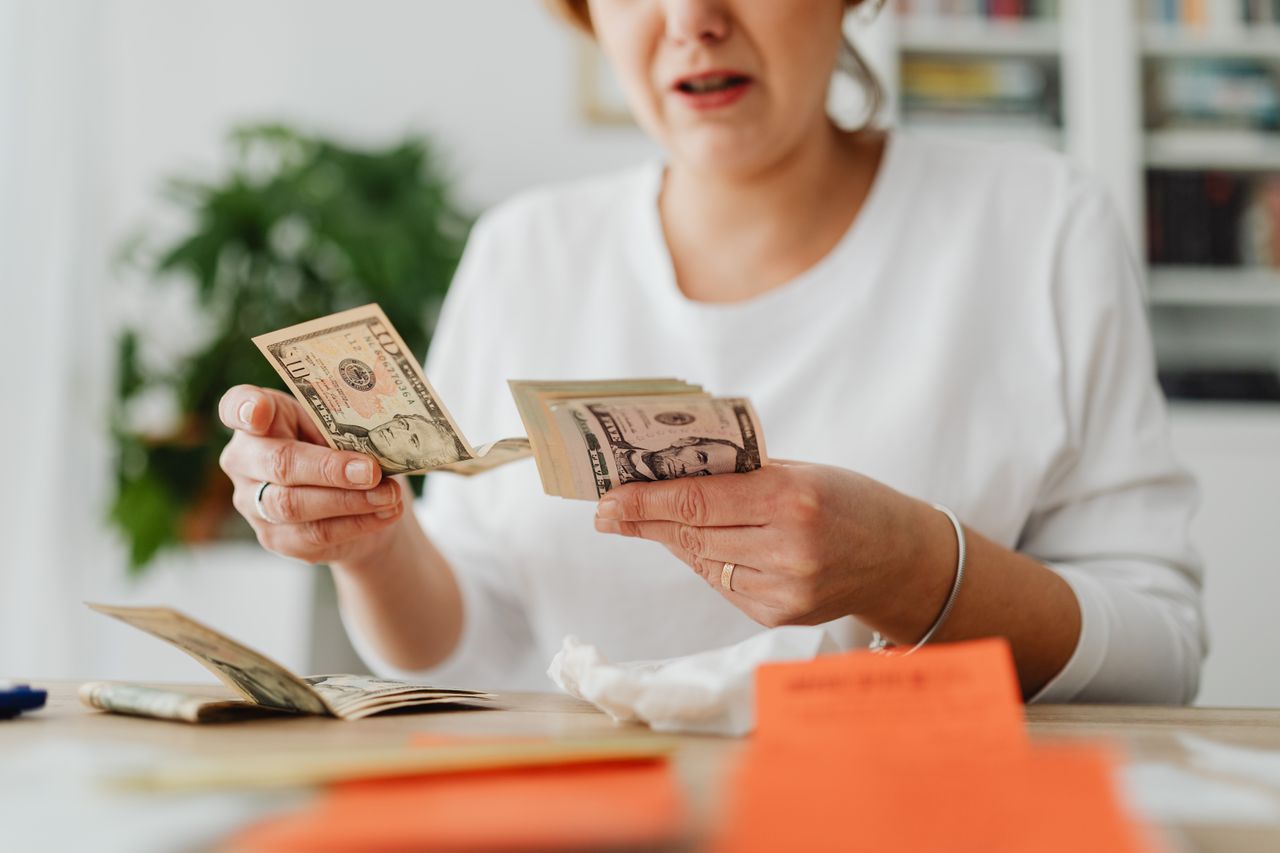 heros-img A woman sits indoors counting cash at her office desk, focusing on finances.