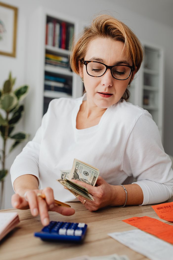 about-us-02 Woman using calculator and handling cash for financial planning at home.
